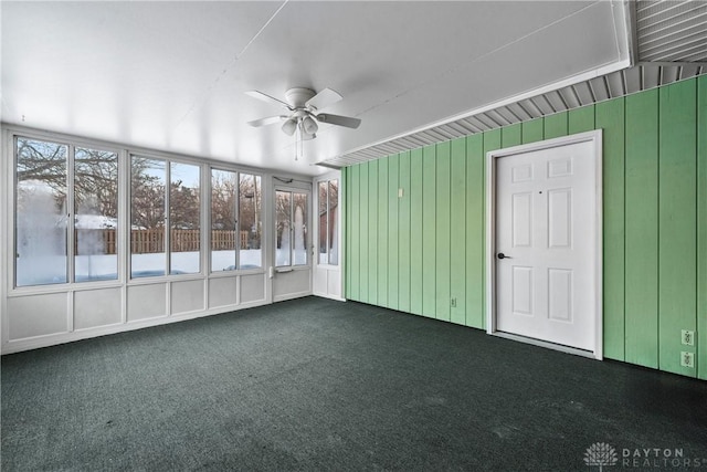 unfurnished room featuring ceiling fan, wood walls, and dark colored carpet