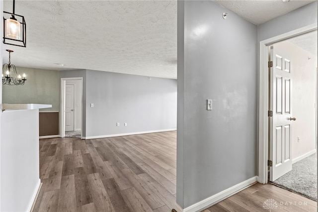 corridor with wood-type flooring, a notable chandelier, and a textured ceiling