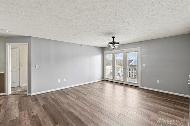 empty room with wood-type flooring, a textured ceiling, and a chandelier