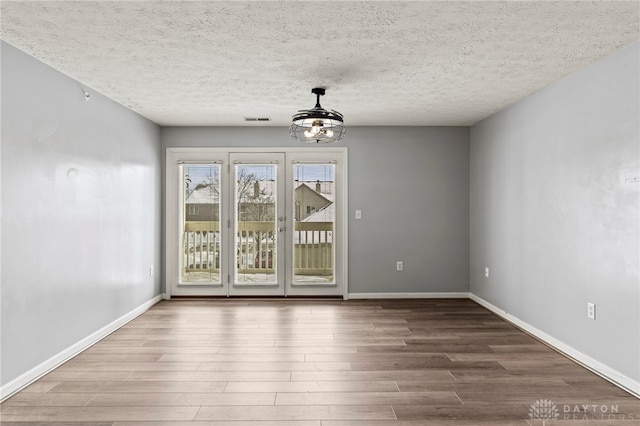 empty room featuring a textured ceiling, hardwood / wood-style flooring, and a notable chandelier