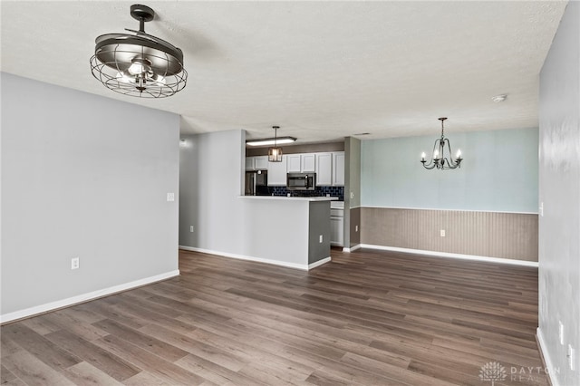 unfurnished living room with a textured ceiling, an inviting chandelier, and wood-type flooring