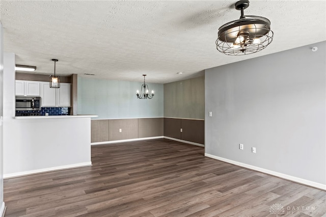 unfurnished living room with a textured ceiling, dark hardwood / wood-style flooring, and a notable chandelier