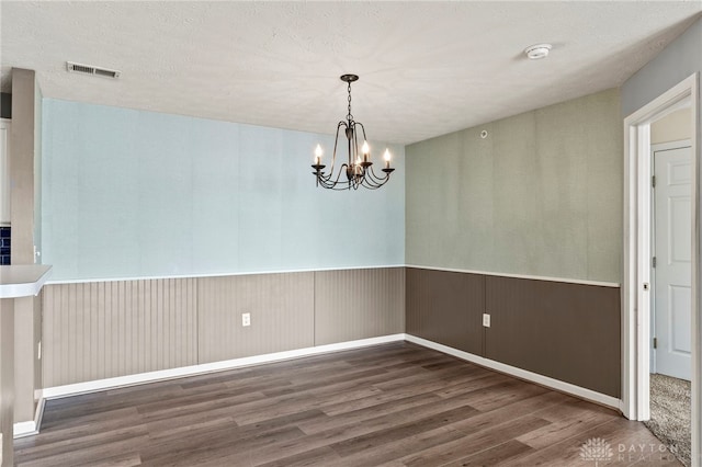 empty room with a notable chandelier, dark hardwood / wood-style flooring, and a textured ceiling