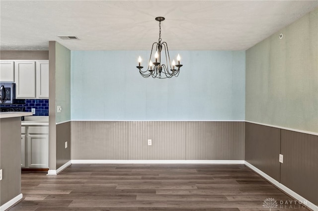 unfurnished dining area featuring dark wood-type flooring and a notable chandelier