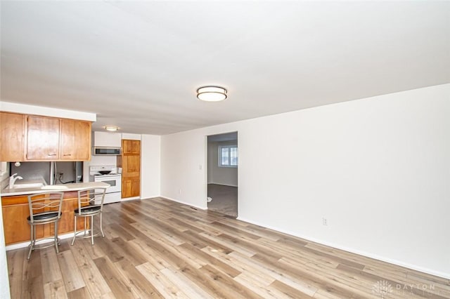 kitchen featuring light hardwood / wood-style floors, a breakfast bar, white electric range oven, and kitchen peninsula