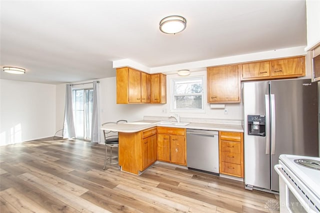 kitchen with light hardwood / wood-style floors, a kitchen bar, kitchen peninsula, stainless steel appliances, and sink