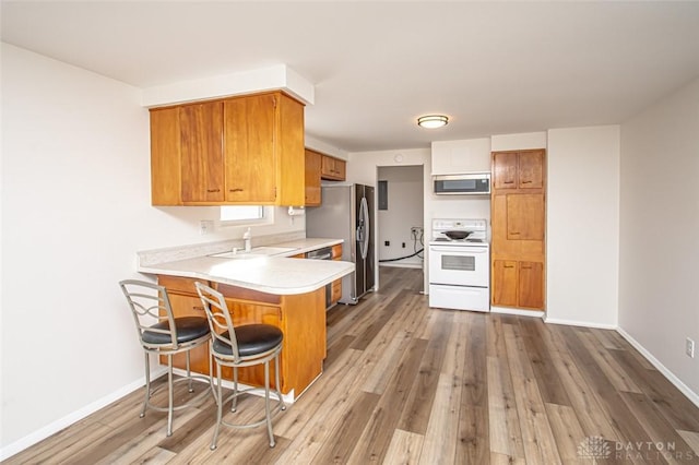 kitchen featuring kitchen peninsula, stainless steel appliances, light hardwood / wood-style flooring, a breakfast bar, and sink