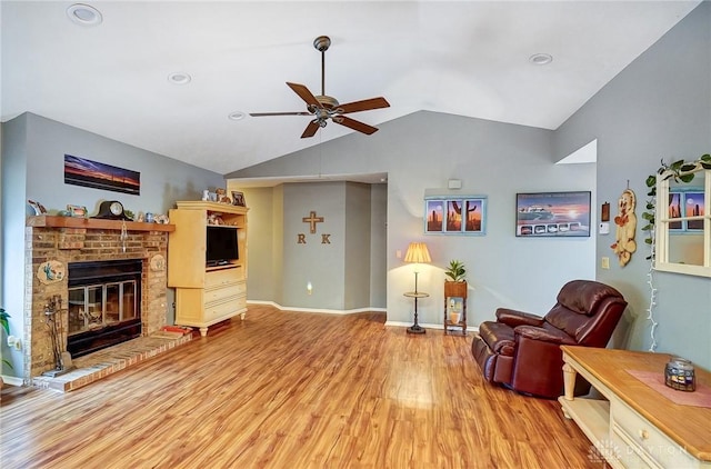 living area featuring ceiling fan, vaulted ceiling, a fireplace, and light hardwood / wood-style flooring