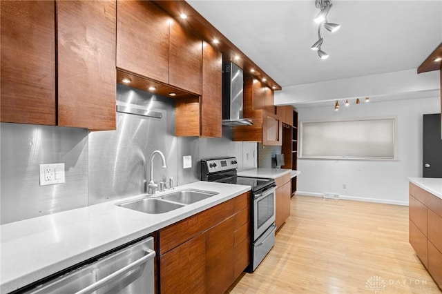 kitchen with appliances with stainless steel finishes, decorative backsplash, wall chimney range hood, light hardwood / wood-style flooring, and sink