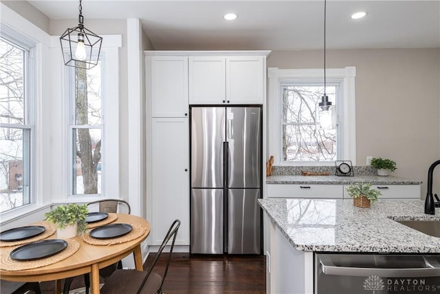 kitchen featuring light stone countertops, hanging light fixtures, appliances with stainless steel finishes, and white cabinets