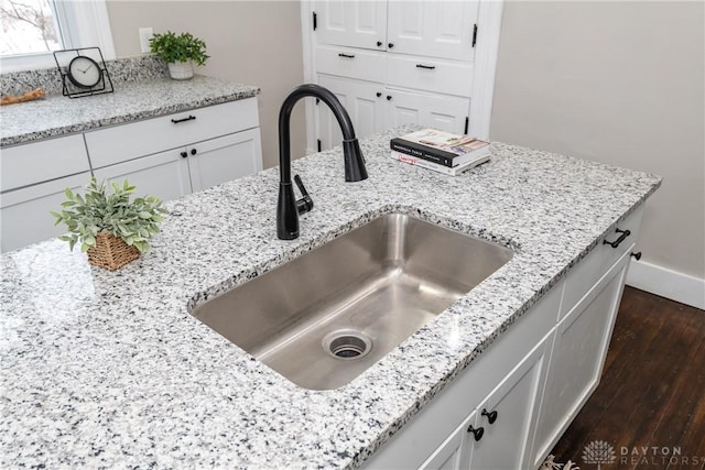 interior details with dark wood-type flooring, sink, white cabinetry, and light stone countertops