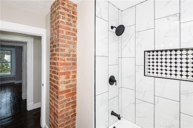 bathroom with hardwood / wood-style flooring, a textured ceiling, and tiled shower / bath