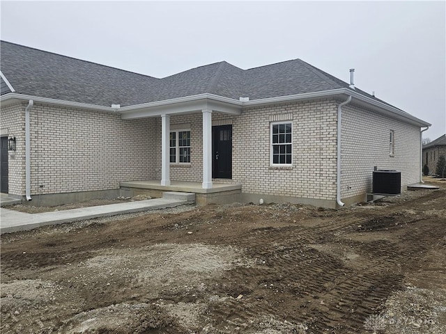 rear view of property featuring a porch, central AC unit, a garage, and roof with shingles