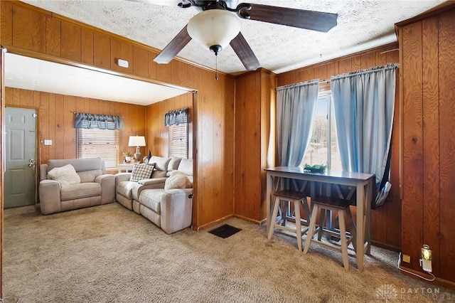 living room featuring a textured ceiling, ceiling fan, carpet flooring, and wooden walls