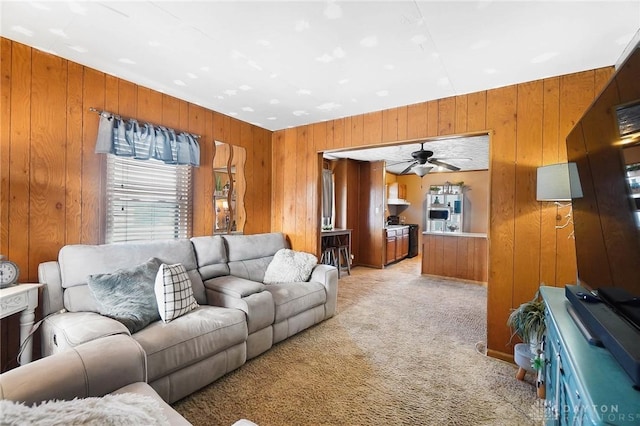 carpeted living room with ceiling fan and wood walls