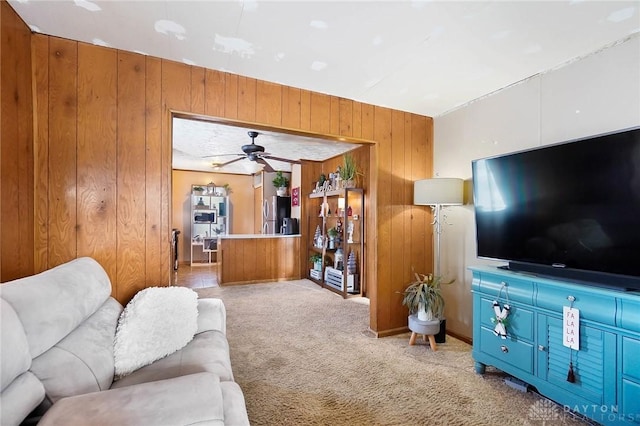 living room with ceiling fan, light carpet, and wooden walls