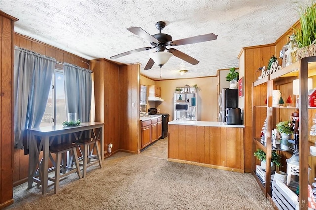 kitchen with ceiling fan, kitchen peninsula, wooden walls, appliances with stainless steel finishes, and light carpet