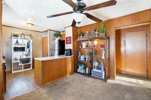 kitchen with light carpet, wood walls, kitchen peninsula, stainless steel appliances, and ornamental molding