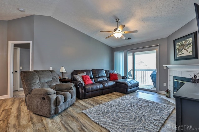 living room with a tiled fireplace, vaulted ceiling, and wood-type flooring