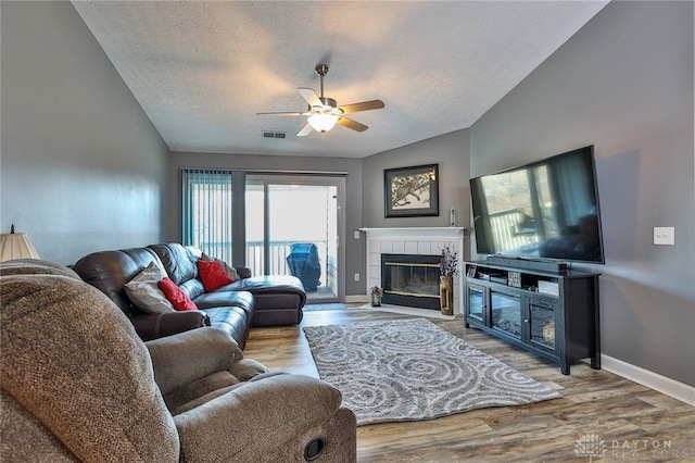 living room with lofted ceiling, hardwood / wood-style flooring, ceiling fan, a textured ceiling, and a tiled fireplace