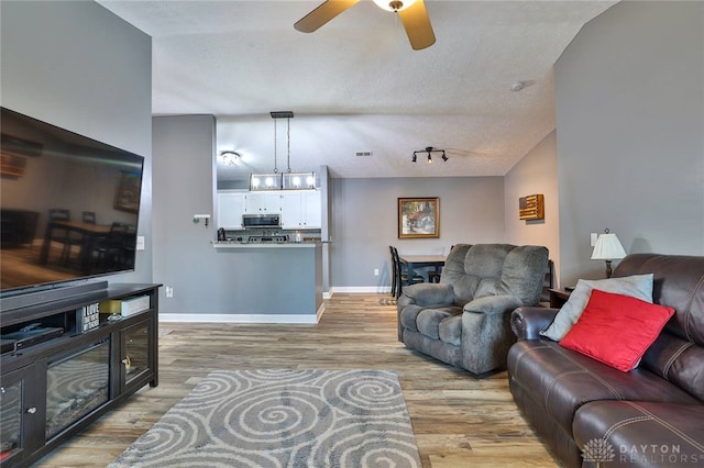 living room featuring ceiling fan, rail lighting, light hardwood / wood-style flooring, and a textured ceiling