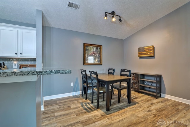 dining room featuring lofted ceiling, light hardwood / wood-style floors, and a textured ceiling