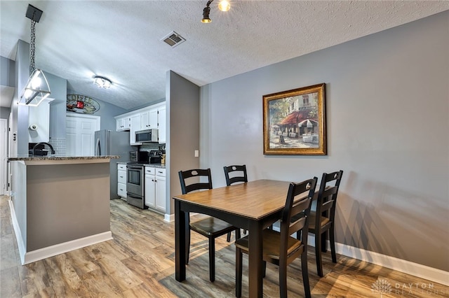 dining room with lofted ceiling, a textured ceiling, and light hardwood / wood-style flooring