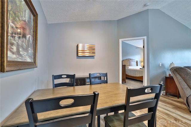 dining room with light hardwood / wood-style flooring, vaulted ceiling, and a textured ceiling