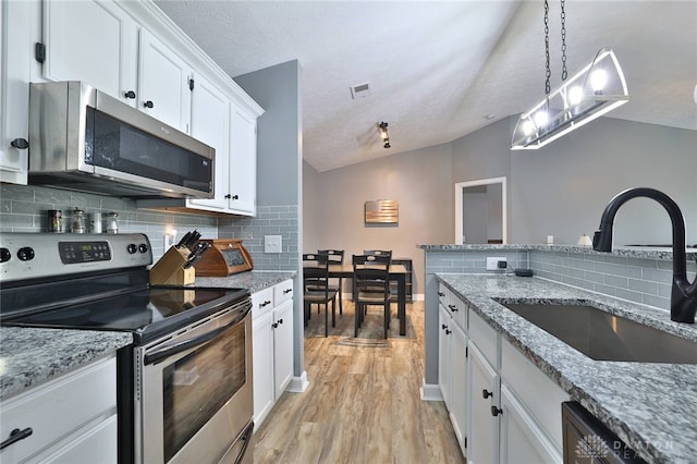 kitchen featuring vaulted ceiling, decorative light fixtures, white cabinetry, sink, and stainless steel appliances