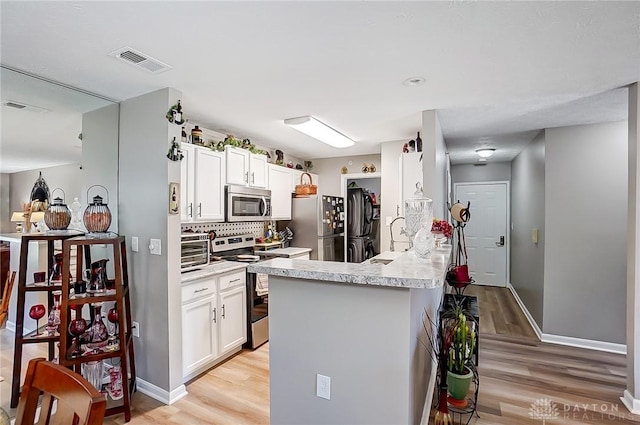 kitchen featuring white cabinets, appliances with stainless steel finishes, light hardwood / wood-style floors, backsplash, and kitchen peninsula