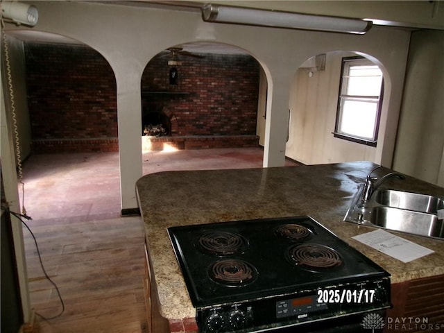 kitchen featuring cooktop, brick wall, stone countertops, and sink