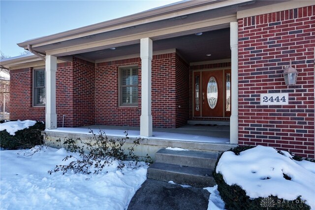 snow covered property entrance with a porch