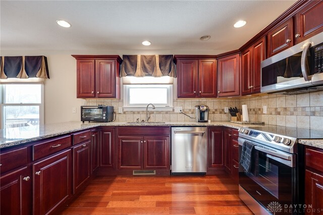 kitchen with light stone countertops, appliances with stainless steel finishes, tasteful backsplash, sink, and hardwood / wood-style flooring