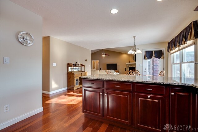 kitchen featuring ceiling fan, dark wood-type flooring, lofted ceiling, pendant lighting, and light stone counters