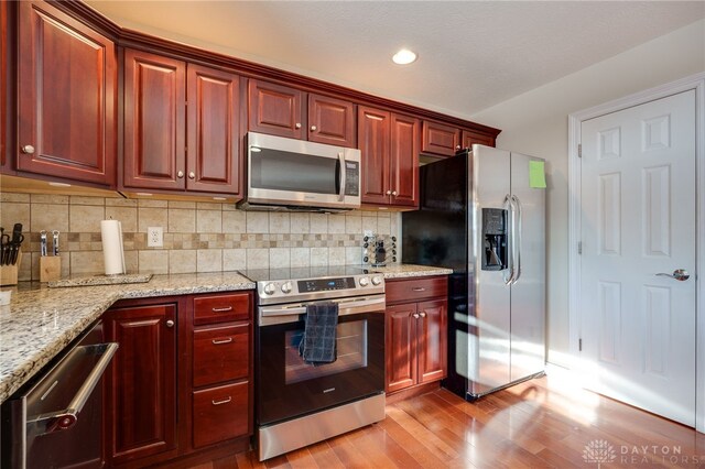 kitchen with decorative backsplash, light stone counters, stainless steel appliances, and light hardwood / wood-style flooring