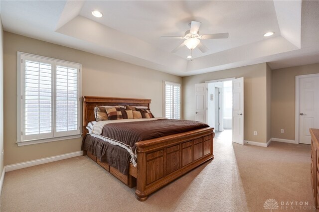 carpeted bedroom featuring ceiling fan, a tray ceiling, and multiple windows