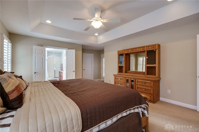 bedroom with connected bathroom, multiple windows, ceiling fan, light colored carpet, and a tray ceiling