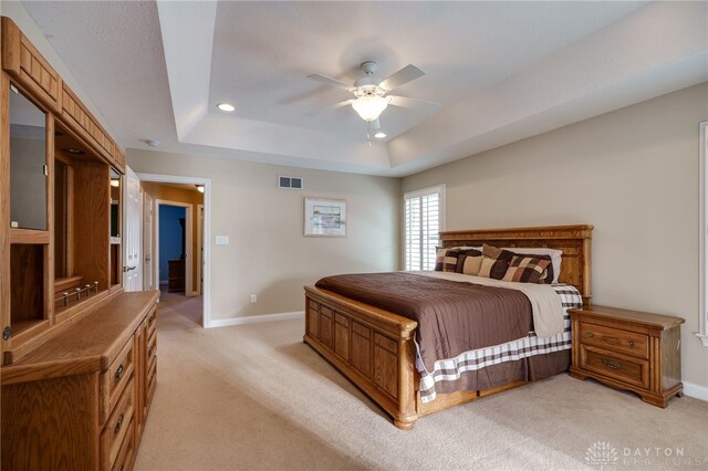 carpeted bedroom with ceiling fan and a tray ceiling