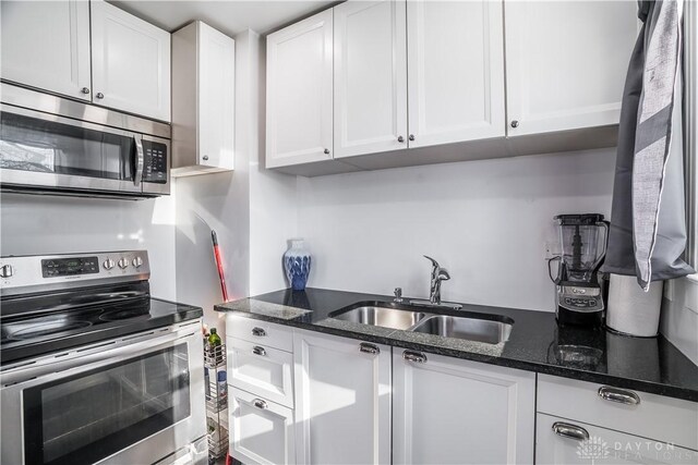 kitchen with appliances with stainless steel finishes, sink, dark stone countertops, and white cabinets