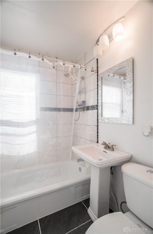 bathroom with toilet, tiled shower / bath combo, and tile patterned flooring