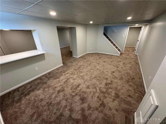 finished below grade area featuring carpet floors, a drop ceiling, baseboards, and stairs