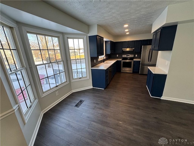 kitchen with dark wood-style flooring, stainless steel appliances, visible vents, light countertops, and under cabinet range hood