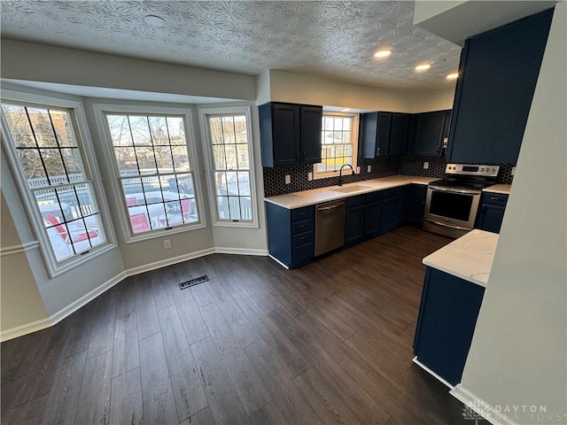 kitchen with dark wood finished floors, stainless steel appliances, light countertops, backsplash, and a sink