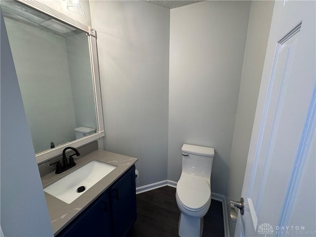 half bath with toilet, baseboards, wood finished floors, and vanity