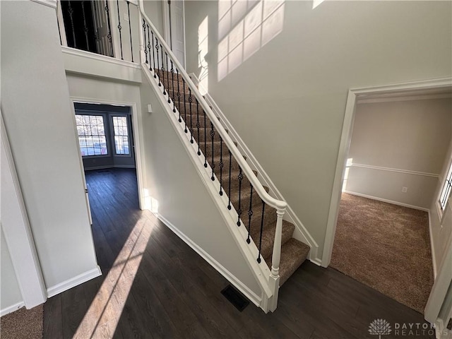 staircase featuring baseboards, a high ceiling, visible vents, and wood finished floors