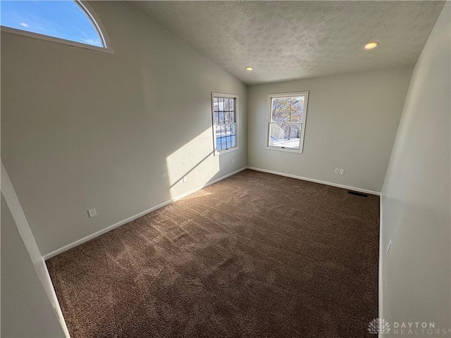 unfurnished room with lofted ceiling, baseboards, dark carpet, and a textured ceiling