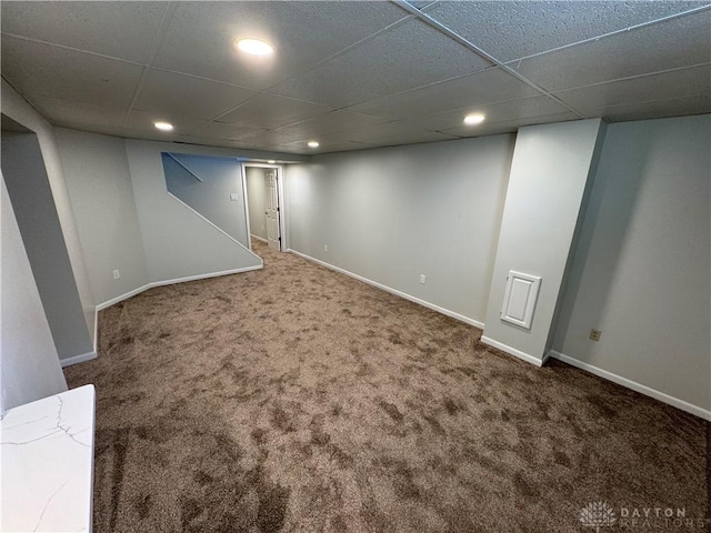 finished below grade area with baseboards, a drop ceiling, and carpet flooring