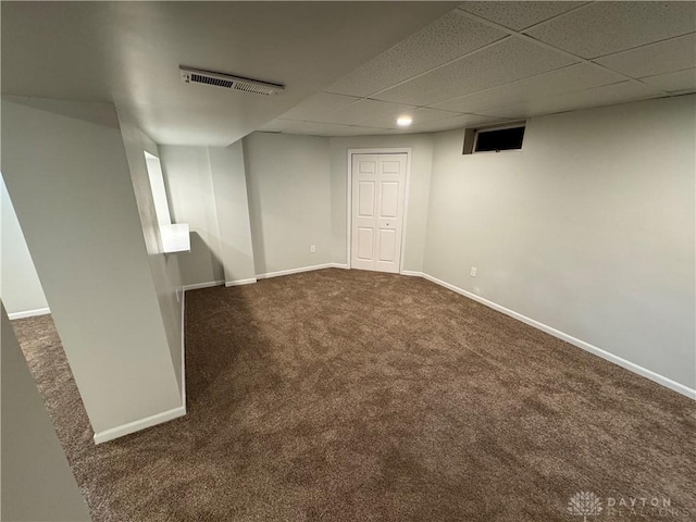 finished basement with visible vents, baseboards, dark colored carpet, and a drop ceiling