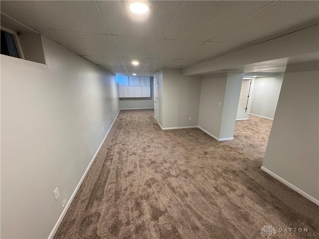 basement featuring light carpet, a drop ceiling, and baseboards