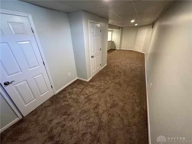 basement featuring dark colored carpet, a paneled ceiling, and baseboards